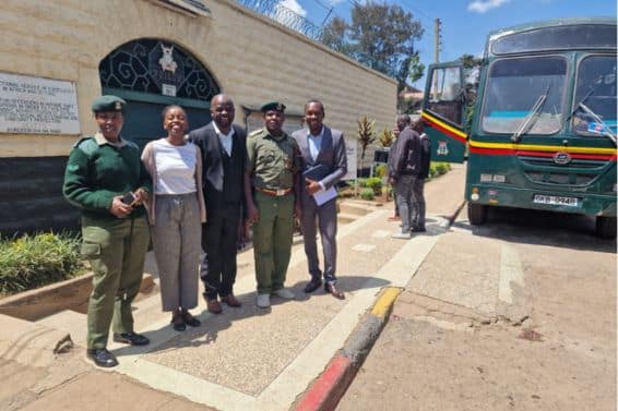 4 men and 1 woman standing in a line outside a prison in Kenya smiling at the camera